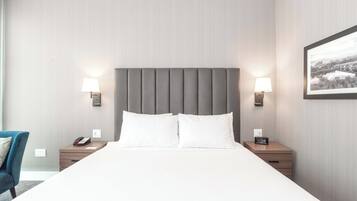 Een hotelkamer met een groot bed, twee nachtkastjes met lampen, een stoel en een lijst aan de muur.