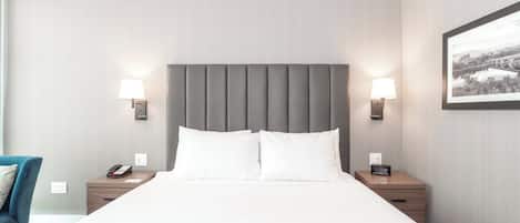 A hotel room with a large bed, two bedside tables with lamps, a chair, and a framed picture on the wall.
