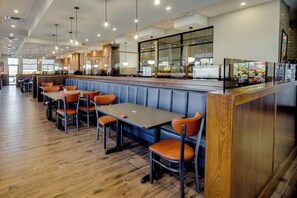 A restaurant with booths and tables, wooden flooring, and pendant lighting. - Sandman Signature Saskatoon South Hotel (Saskatoon)