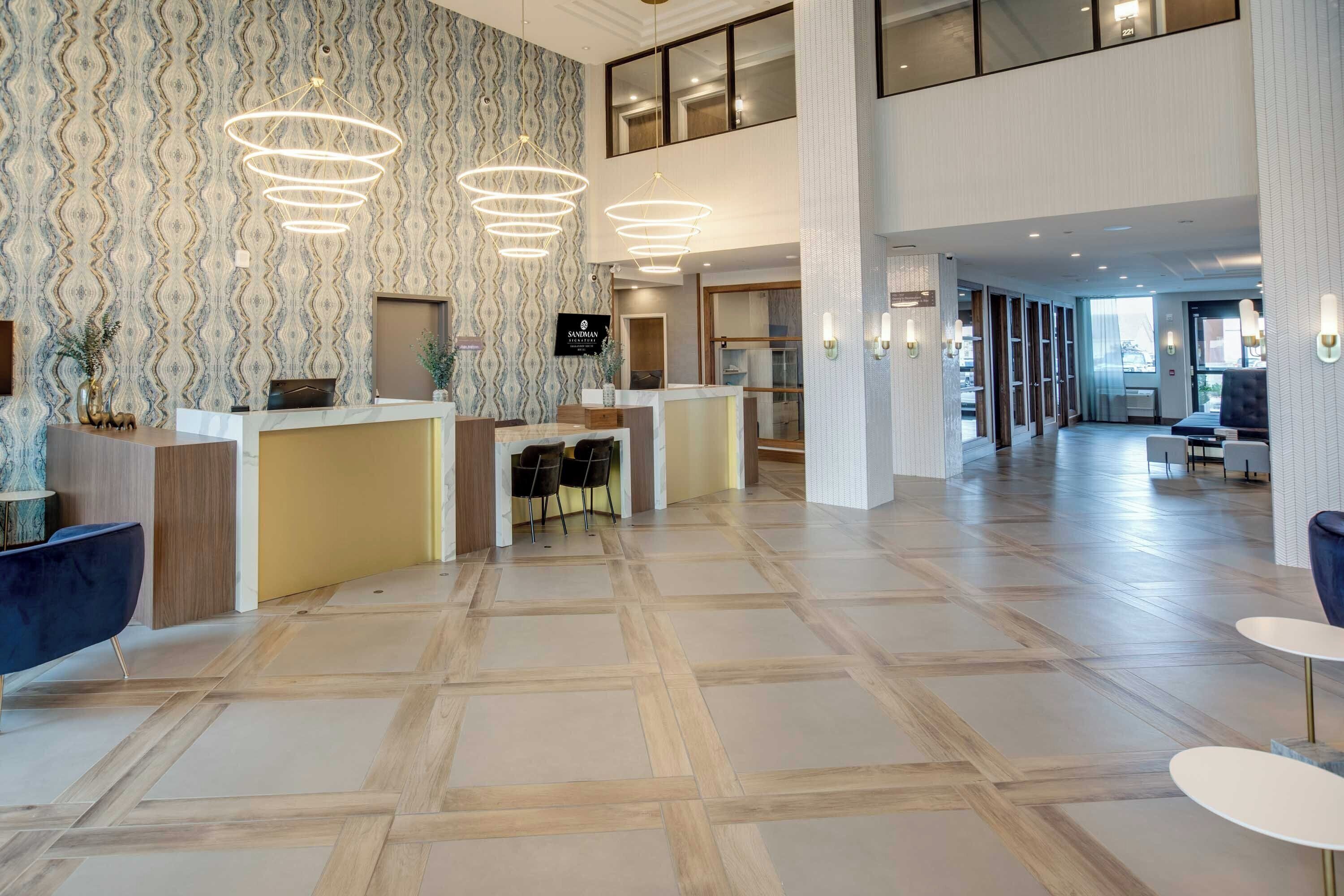 A hotel lobby with a reception desk, patterned wallpaper, and modern lighting fixtures.