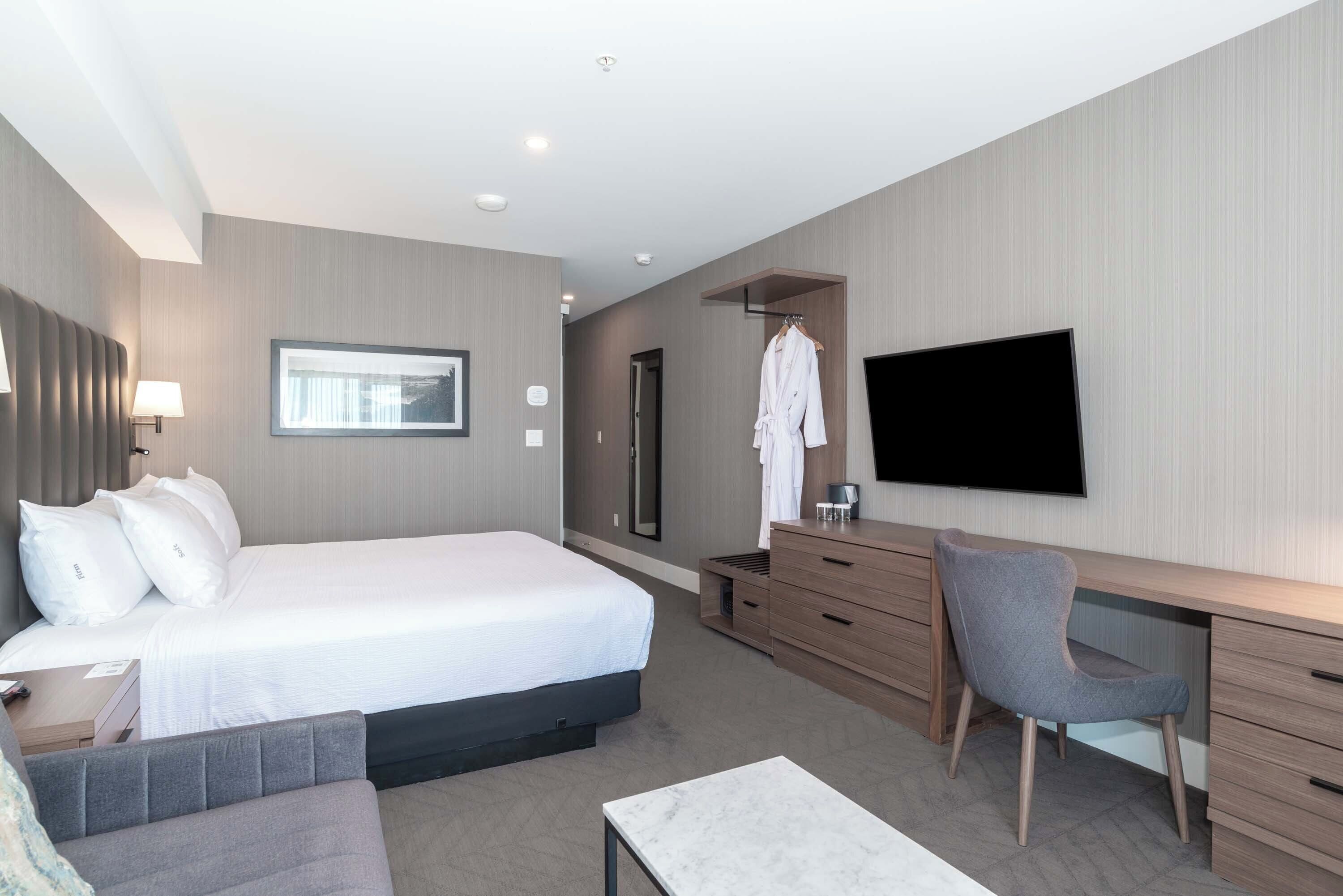Una habitación de hotel moderna con una cama grande, un escritorio, una silla, un televisor y un armario.