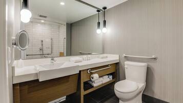 Une salle de bain moderne avec un lavabo blanc, un miroir et des toilettes. Il y a deux luminaires au plafond et un porte-serviettes.