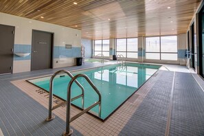 An indoor swimming pool with clear poolside railings, a tiled floor, and large windows offering a view of the sky. - Sandman Signature Saskatoon South Hotel (Saskatoon)