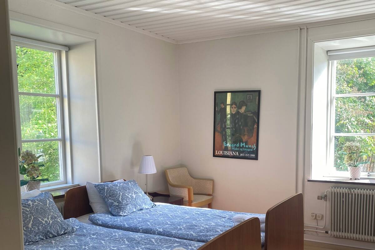 A bedroom with two beds, a chair, a radiator, and a poster on the wall.