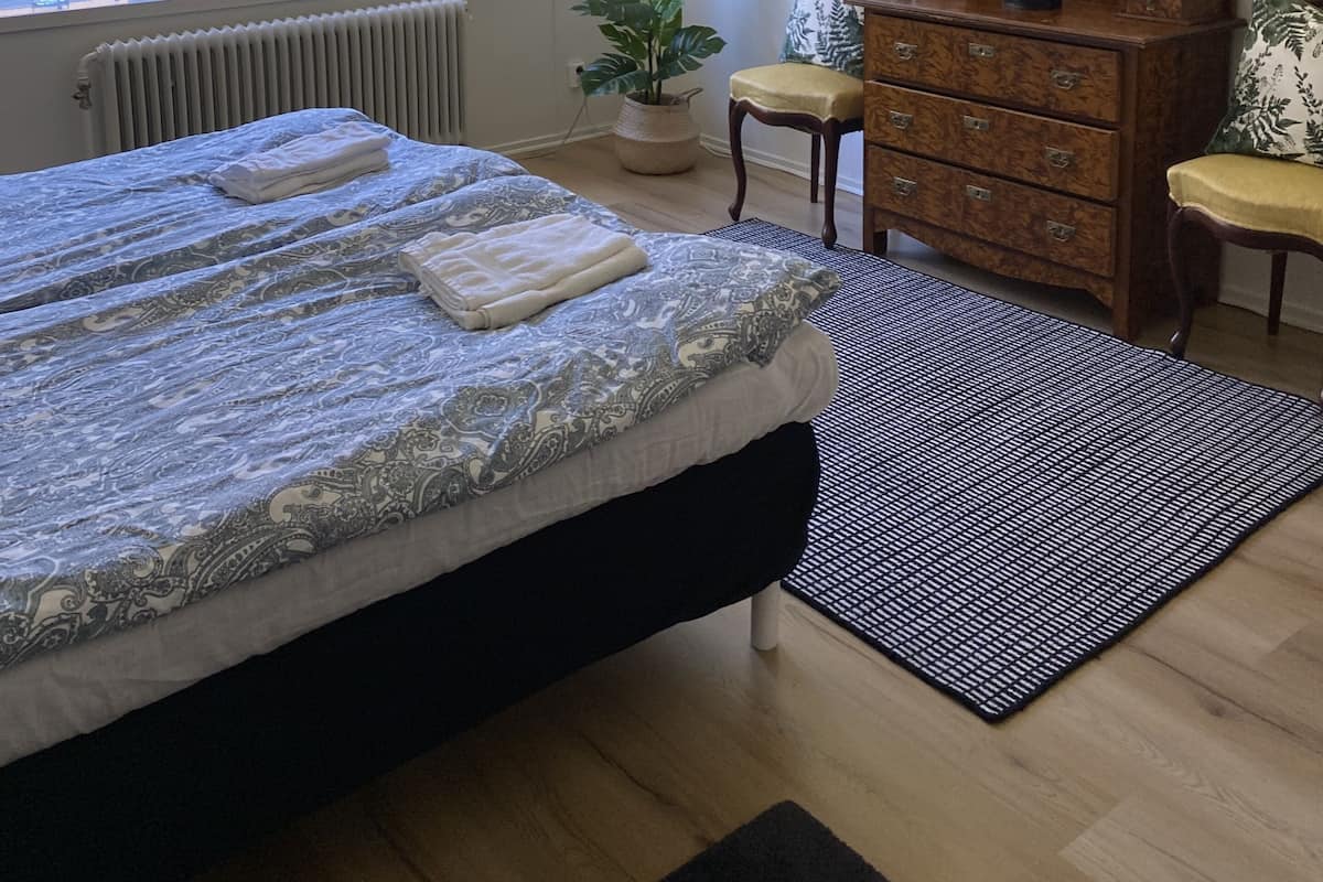 A bedroom with a bed, dresser, chair, potted plants, and a window.