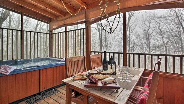 Una terraza de madera con un jacuzzi, una mesa preparada para comer y vistas a árboles entre los barrotes.