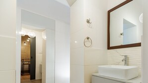 Un baño moderno con un tocador blanco, un espejo grande y suelo de madera.