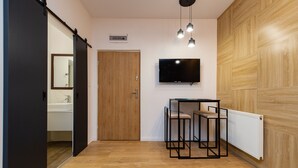 Una habitación moderna con suelo de madera, una puerta corredera, un televisor fijado a la pared y un radiador.