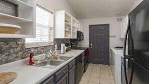 A modern kitchen with white cabinets, a black refrigerator, and a gray backsplash. - Charming 3bdr home 10 min to downtown! (Nashville)