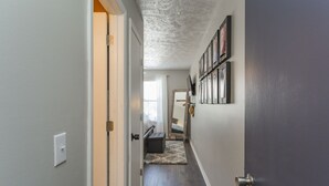 A hallway with a wooden floor, a rug, a bed, and a wall with framed pictures. - Charming 3bdr home 10 min to downtown! (Nashville)