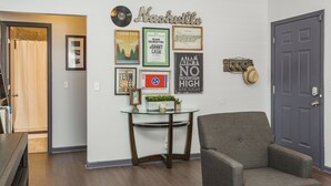 A living room with a glass-top coffee table, a gray armchair, and various framed pictures on the wall. - Charming 3bdr home 10 min to downtown! (Nashville)