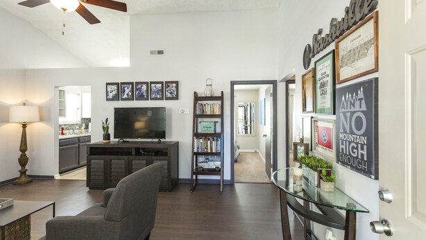 A modern living room with a flat-screen TV, a bookshelf, and a glass coffee table. - Charming 3bdr home 10 min to downtown! (Nashville)