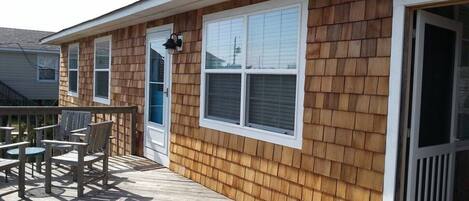 A wooden house with a deck, a sliding glass door, and a window with blinds.