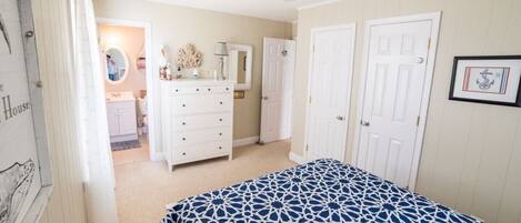 A bedroom with a bed, a dresser, a ceiling fan, and two doors.