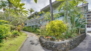 A hotel with a stone retaining wall, lush tropical vegetation, and a curved driveway leading to the entrance. - Kailua-Kona Studio - Walk to Hale Halawai Park! (Kailua-Kona)