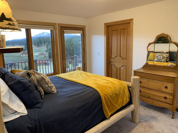 A bedroom with a bed, a dresser, and a large window with a view of mountains.