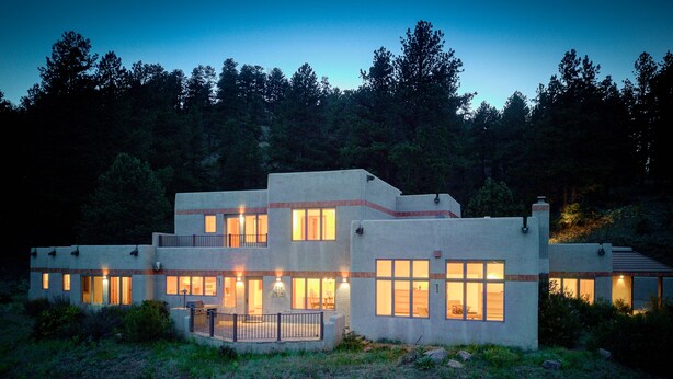 Une maison moderne à deux étages, dotée de nombreuses fenêtres et d’un éclairage extérieur soigné, particulièrement visible au crépuscule.