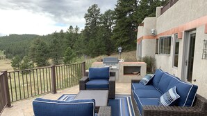 Une terrasse avec des meubles en osier, un barbecue et un mur en pierre.