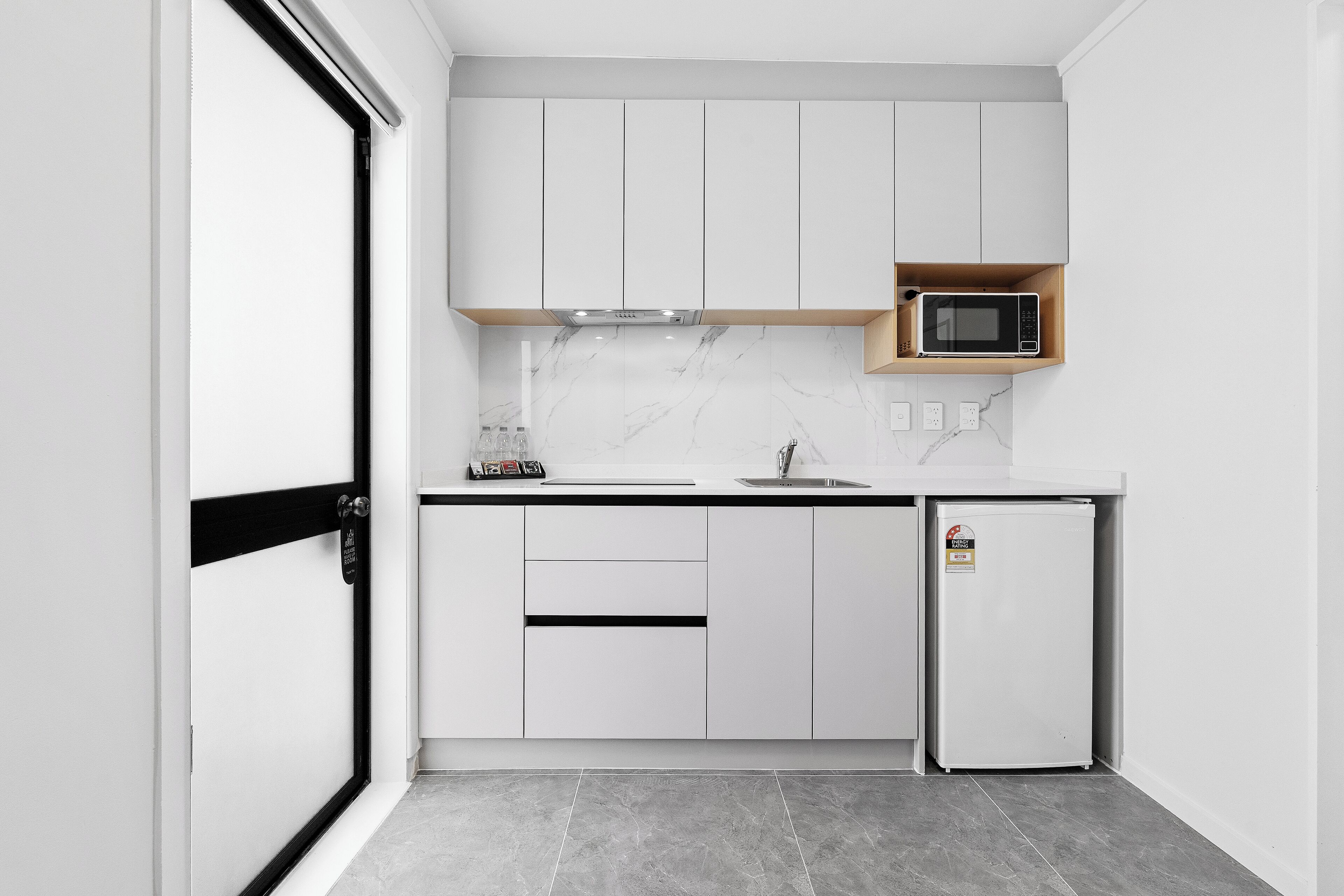 A modern kitchen with white cabinets, a built-in microwave, and a refrigerator.