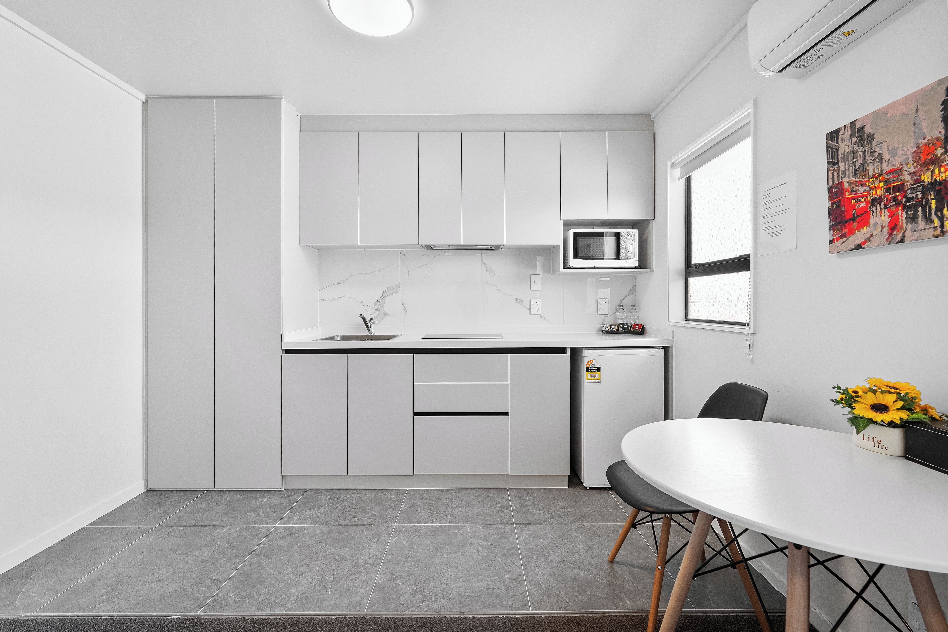 Una cocina moderna con armarios blancos, un microondas y un comedor con una mesa y sillas.