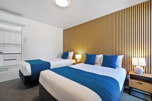 A hotel room with two beds, a wooden slat wall, a desk, and a nightstand with lamps.