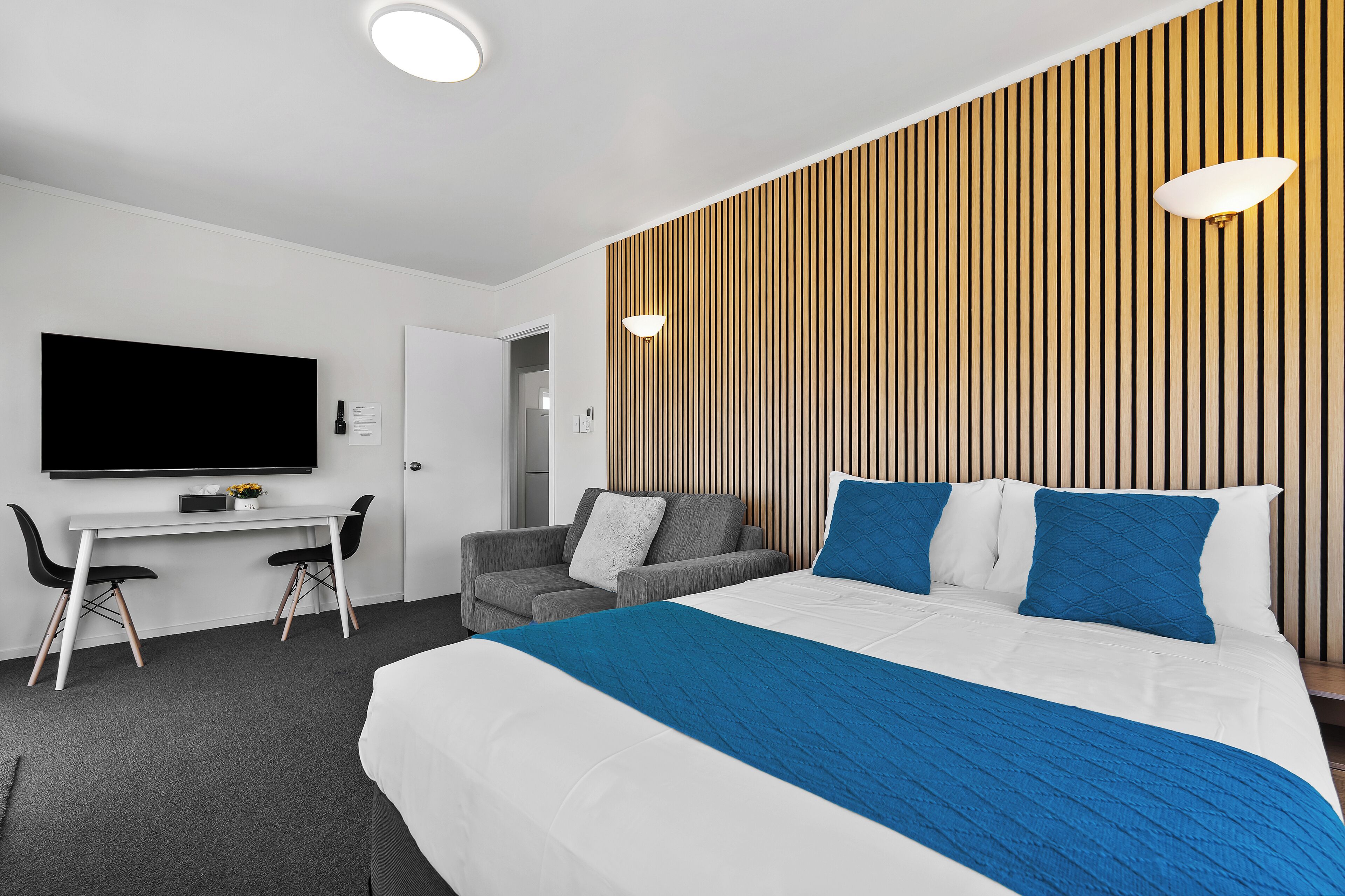 Une chambre d’hôtel moderne, dotée d’un grand lit, d’un bureau, d’un canapé et d’un téléviseur fixé au mur.