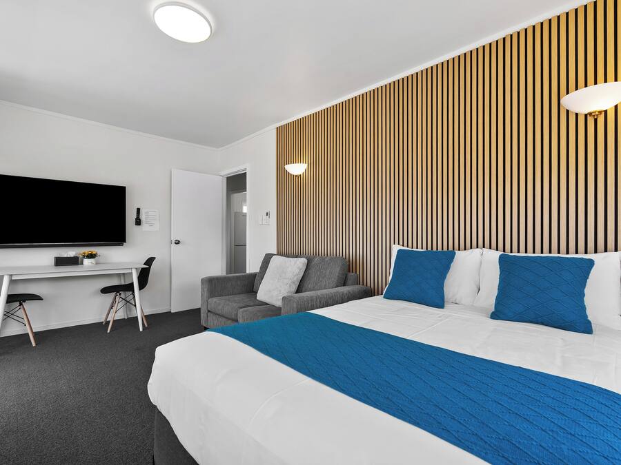 A modern hotel room with a large bed, a desk, a sofa, and a TV mounted on the wall.
