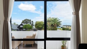 A balcony with wicker furniture, a potted plant, and a view of houses and trees. - Summer Inn Motel (Orewa)