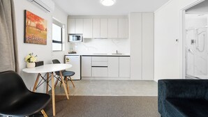 A modern kitchen with white cabinets, a microwave, and a dining area with a table and chairs. - Summer Inn Motel (Orewa)