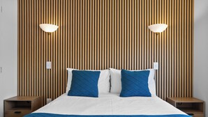 A neatly made bed with a blue quilt, two matching pillows, and a wooden slat wall behind it. There are two bedside tables with lamps on either side of the bed. - Summer Inn Motel (Orewa)