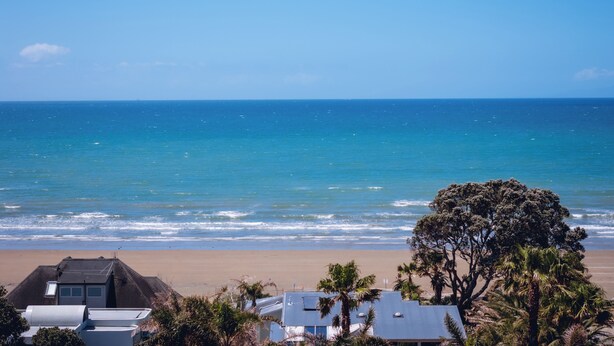 A coastal view with a beach, ocean, and a residential area with houses and trees. - Summer Inn Motel (Orewa)