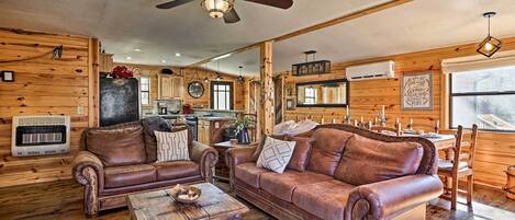 L’intérieur d’un chalet confortable, avec des murs en bois, une table à manger en bois, deux canapés en cuir, un ventilateur de plafond et une grande fenêtre.