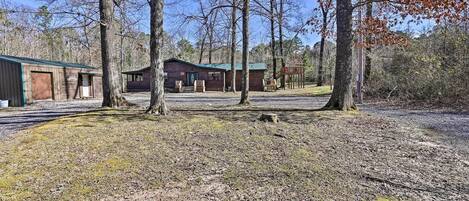 A rustic cabin with a green roof, surrounded by trees and a gravel driveway.