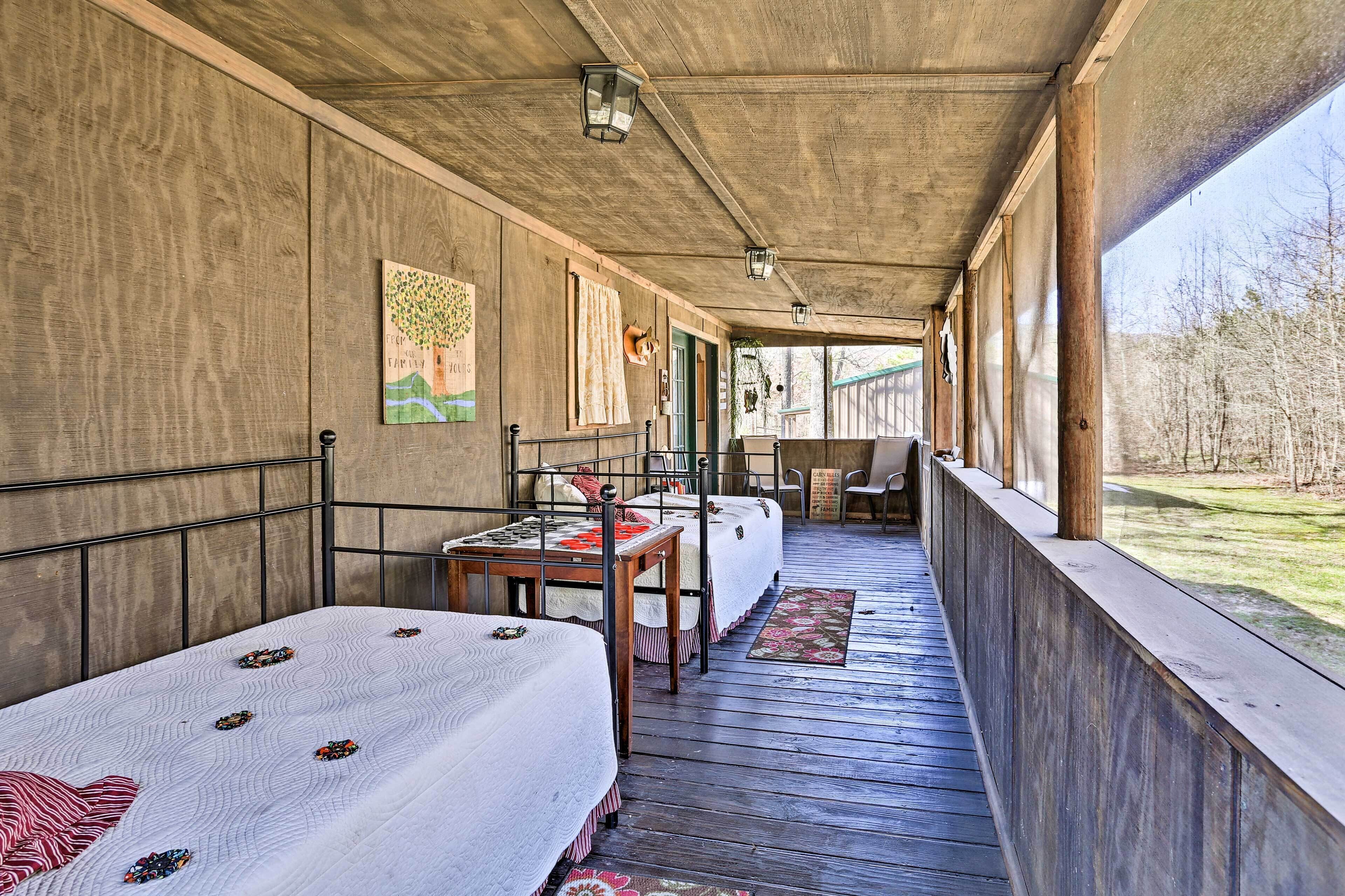 A covered porch with two beds, a table, and a chair.