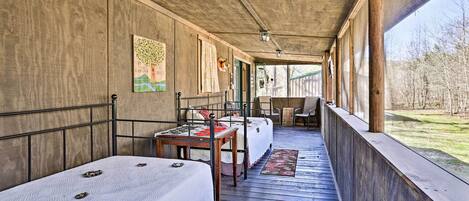 A covered porch with two beds, a table, and a chair.