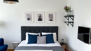 Een moderne slaapkamer met een groot bed, een glazen bijzettafeltje, een televisie en kunst aan de muur.