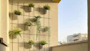 Een balkon met een rij bloempotten, twee houten krukken en een vloer met een patroon.