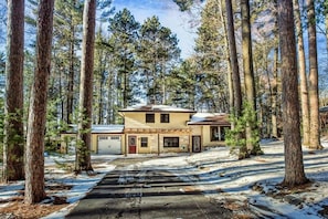 A two-story building surrounded by tall pine trees with a snow-covered ground.