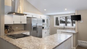 Una cocina moderna con encimeras de granito, electrodomésticos de acero inoxidable, muebles de cocina blancos y un horno empotrado.