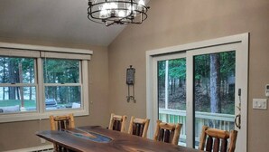 Un comedor con una mesa de madera larga, bancos y sillas. Hay ventanas amplias con vistas a árboles y una terraza afuera.