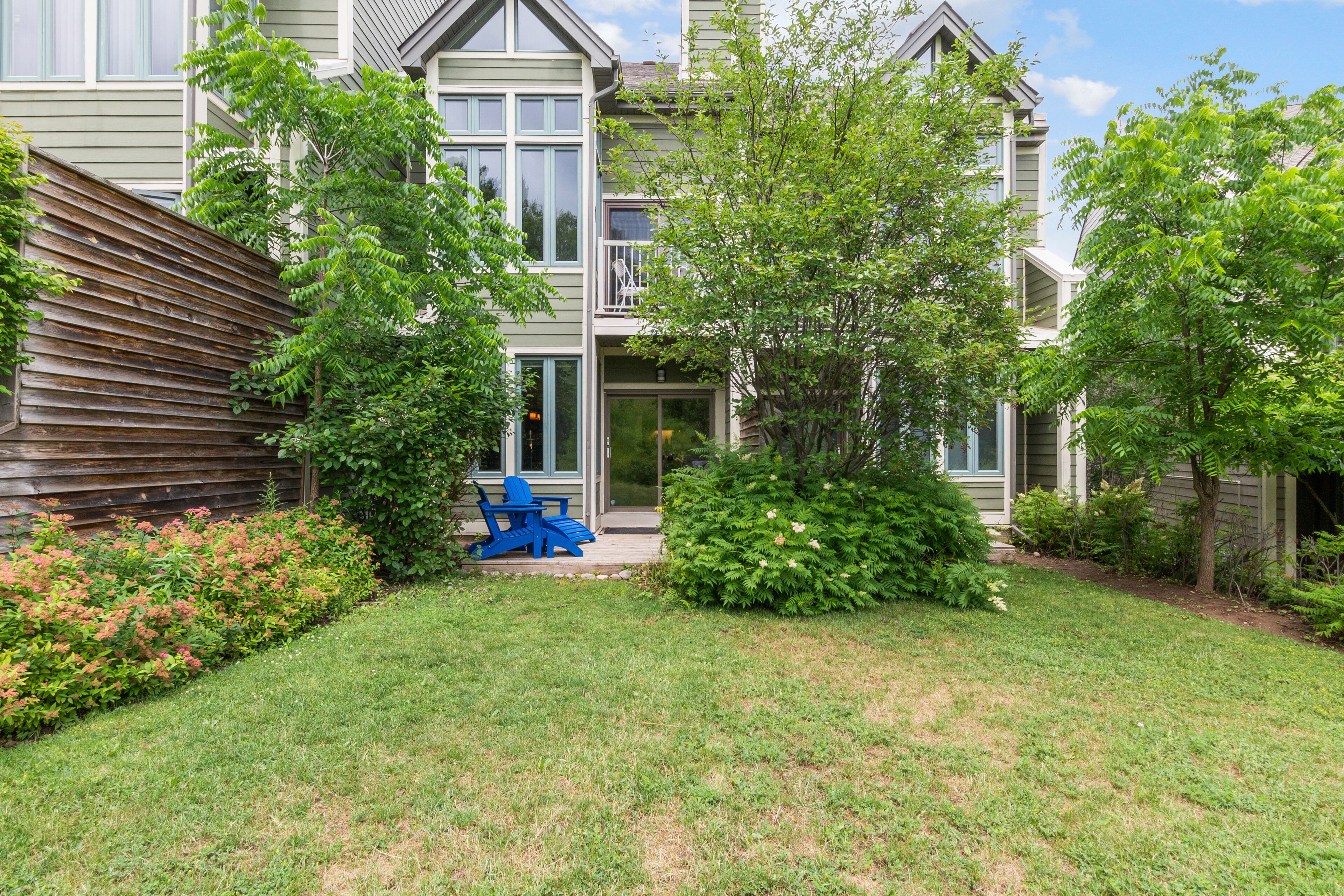 A two-story house with a well-maintained lawn, a patio with outdoor furniture, and a variety of shrubs and trees.