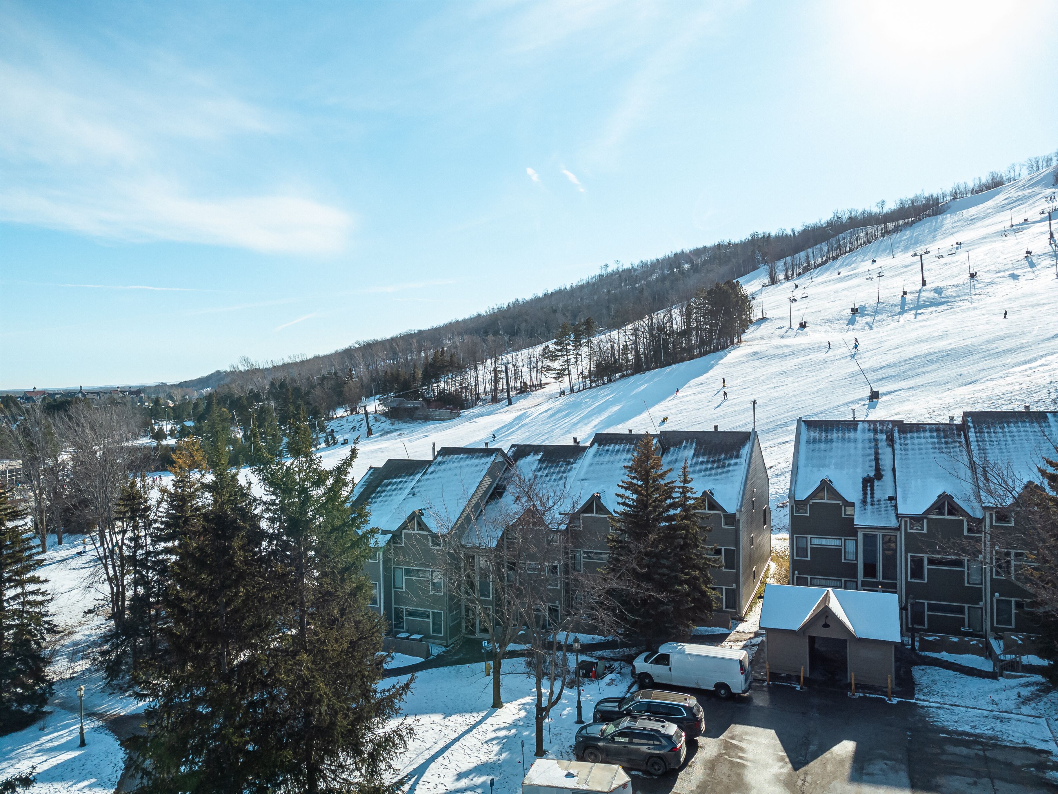 A ski resort with buildings, a parking area, and a snowy landscape.