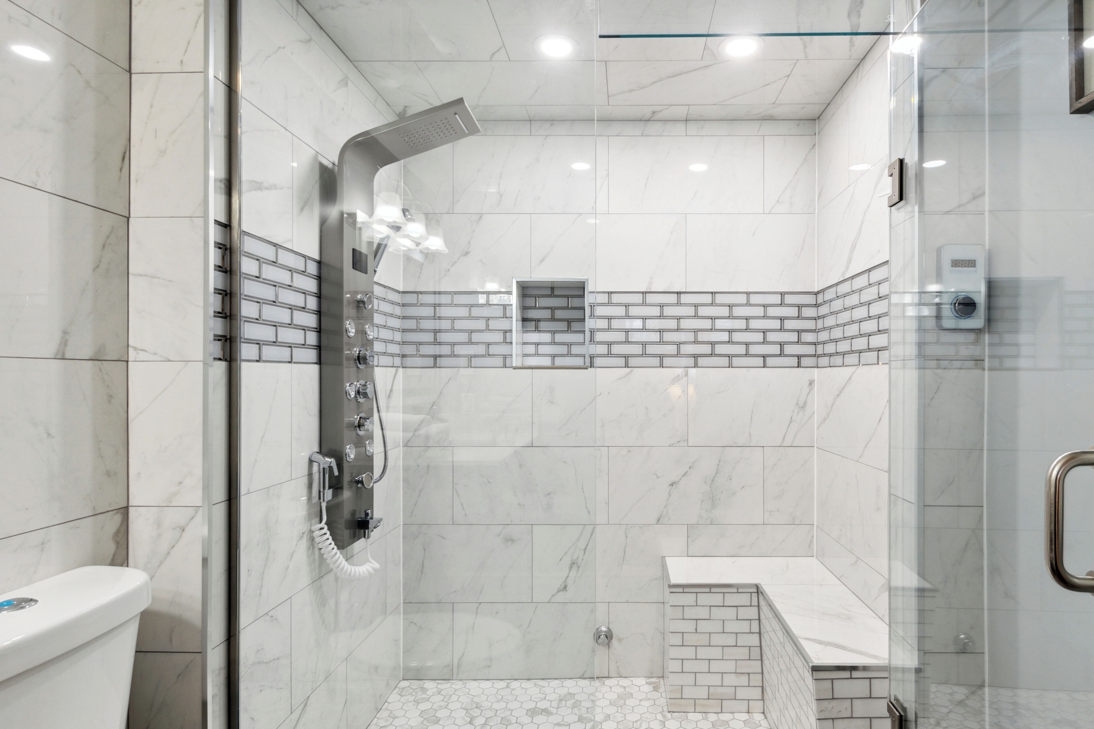 Ein modernes Badezimmer mit einer gläsernen Dusche, weißen Marmorfliesen und einer kleinen Waschtisch-Ecke.