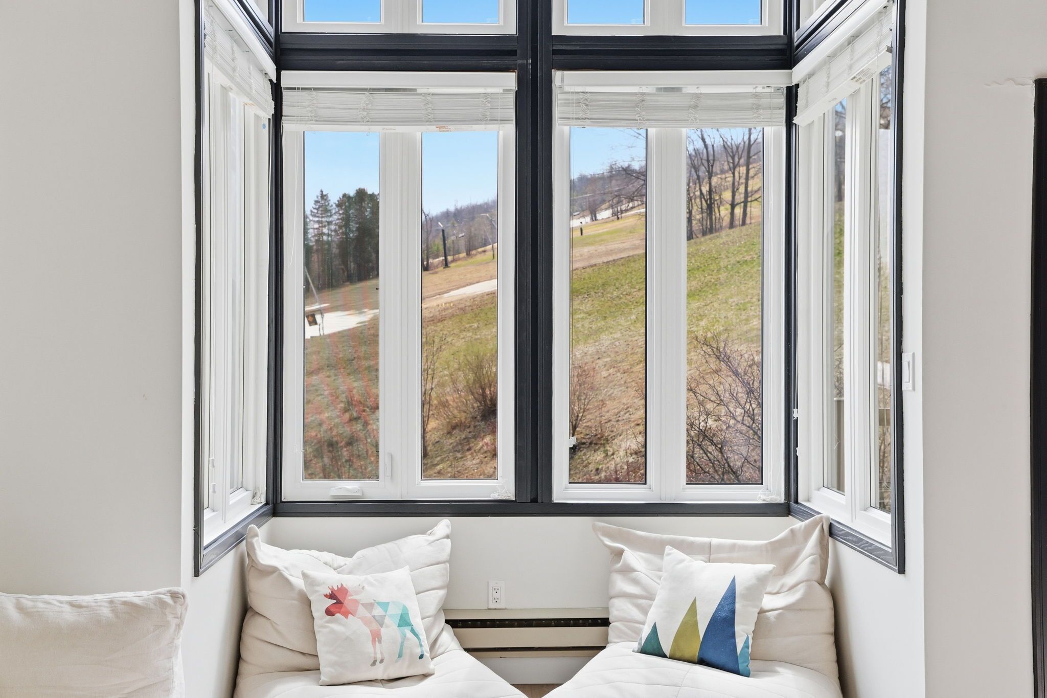 A room with a large window offering a view of a grassy field and trees.
