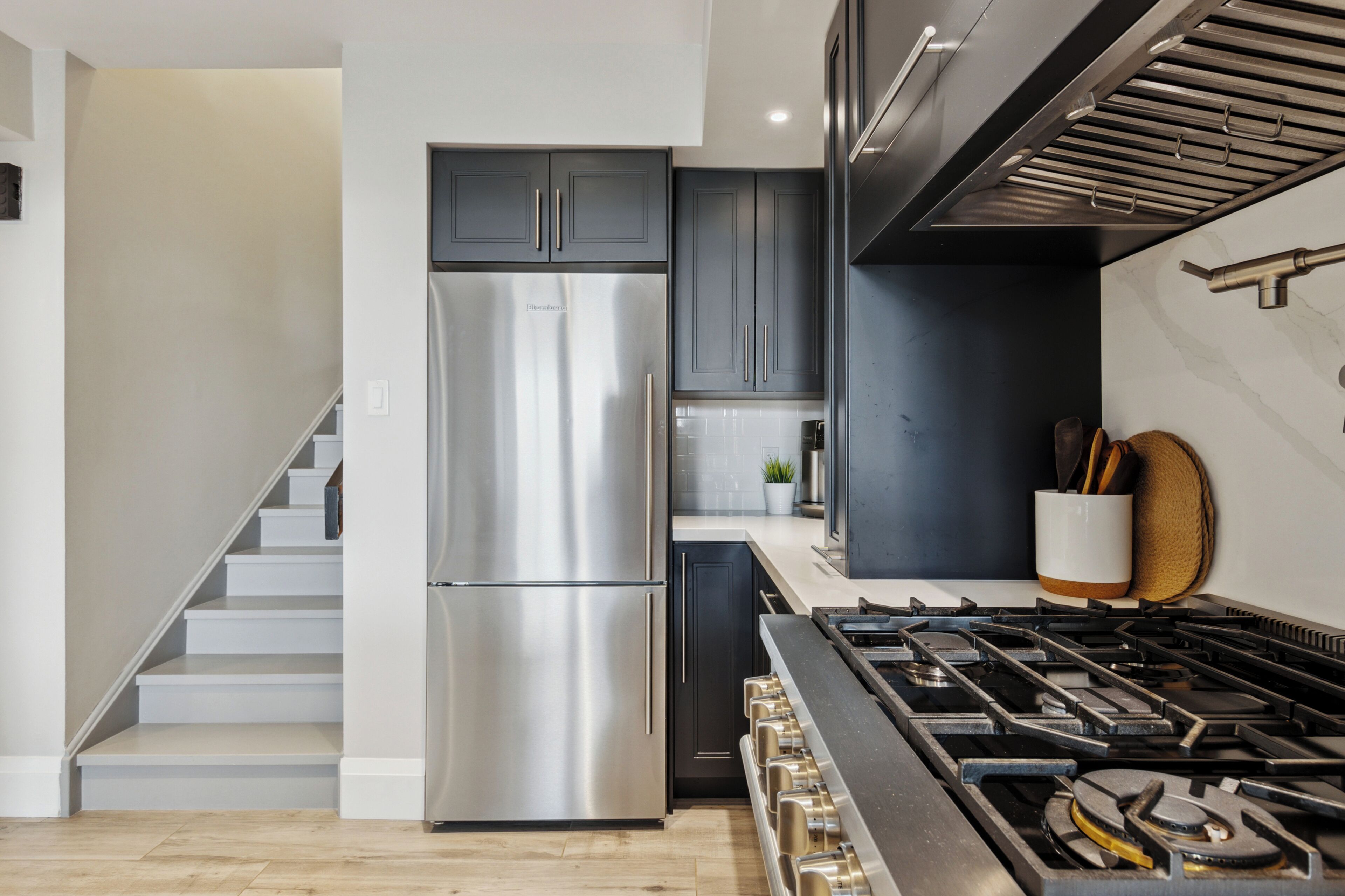 A modern kitchen with a stainless steel refrigerator, dark cabinetry, a gas stove, and a wooden countertop.