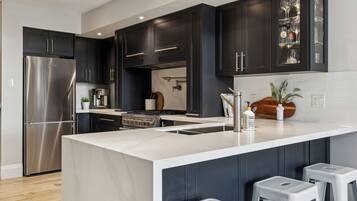 A modern kitchen with dark cabinetry, stainless steel appliances, a marble countertop, and a central island with stools.