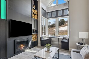 Una sala moderna con chimenea, televisor de pantalla plana, comedor y ventanas amplias que ofrecen vistas al exterior.