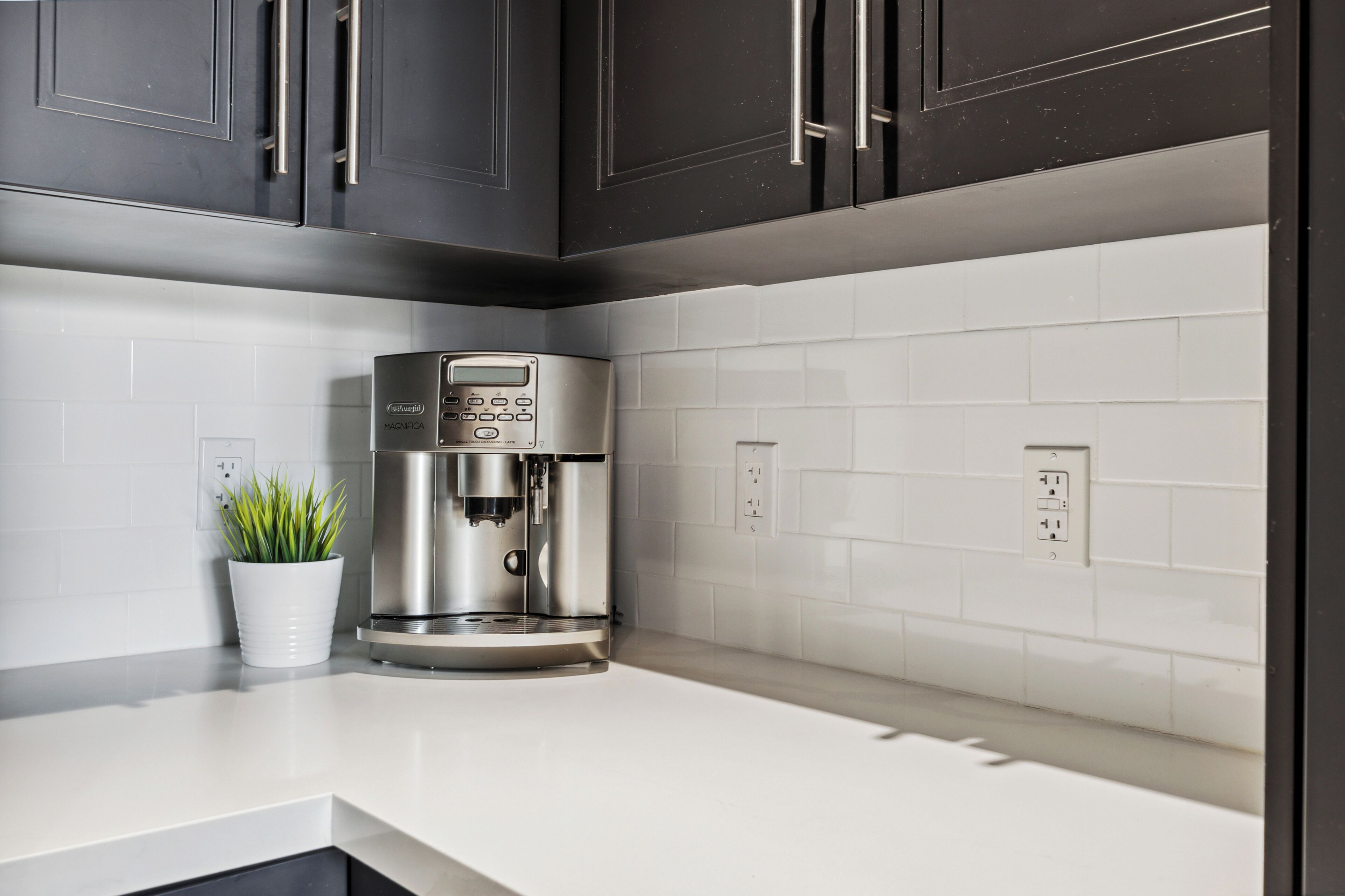 A modern kitchen with dark cabinets, a white countertop, and a coffee machine.