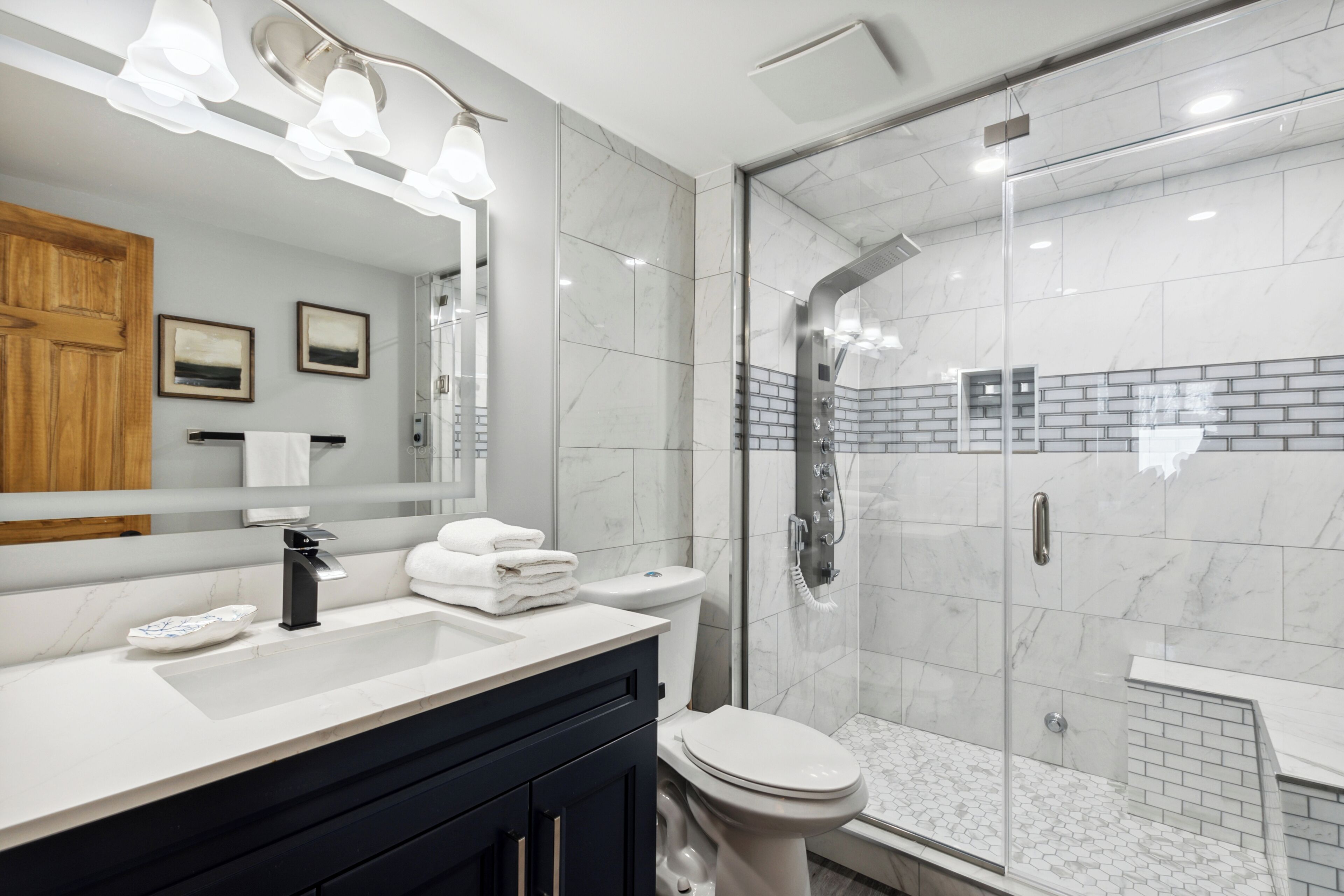 Un baño moderno con un espejo grande, un lavamanos, un inodoro y una ducha con mampara de vidrio.