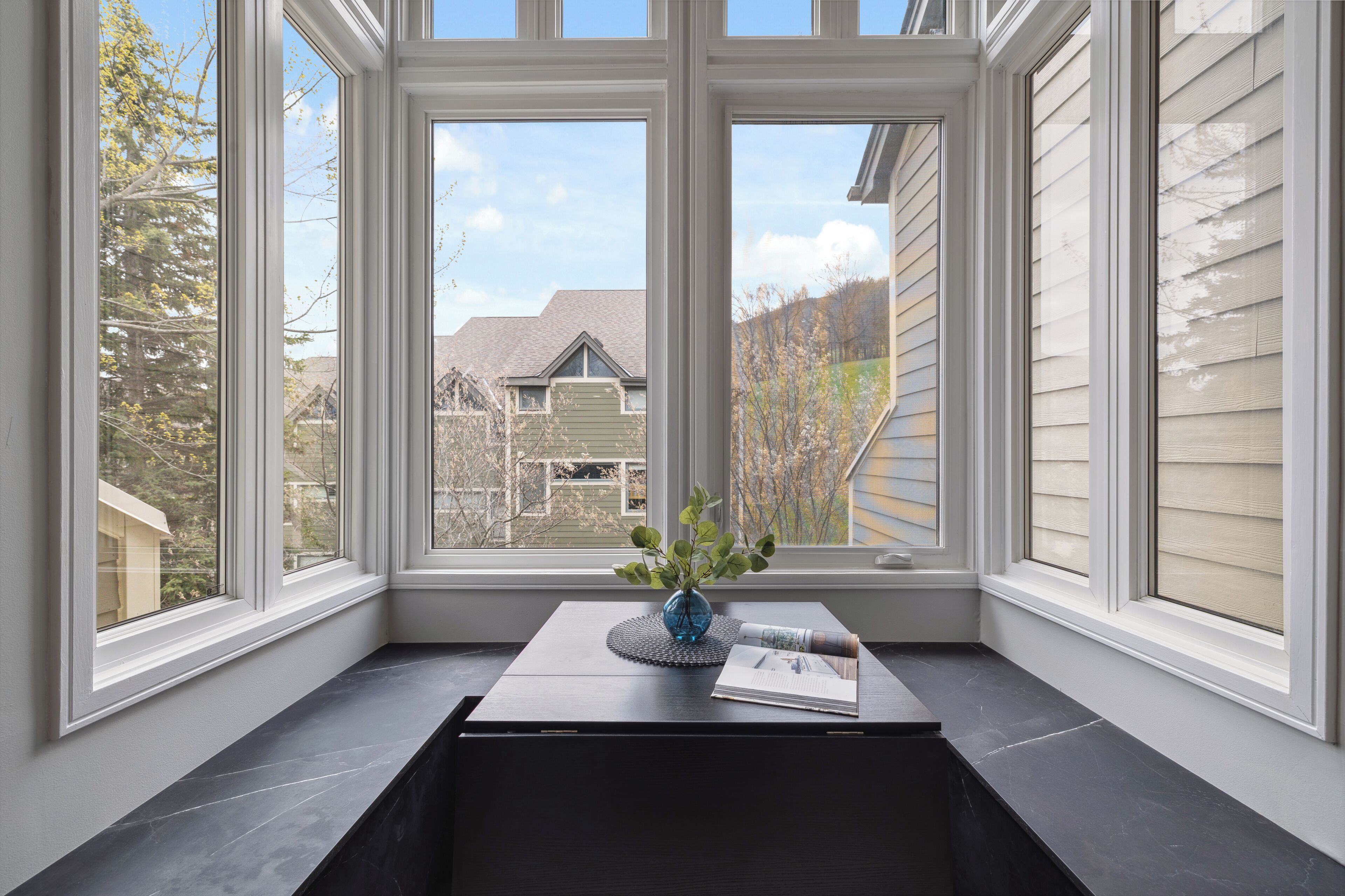 A corner with a window seat, a vase with flowers, and a magazine.
